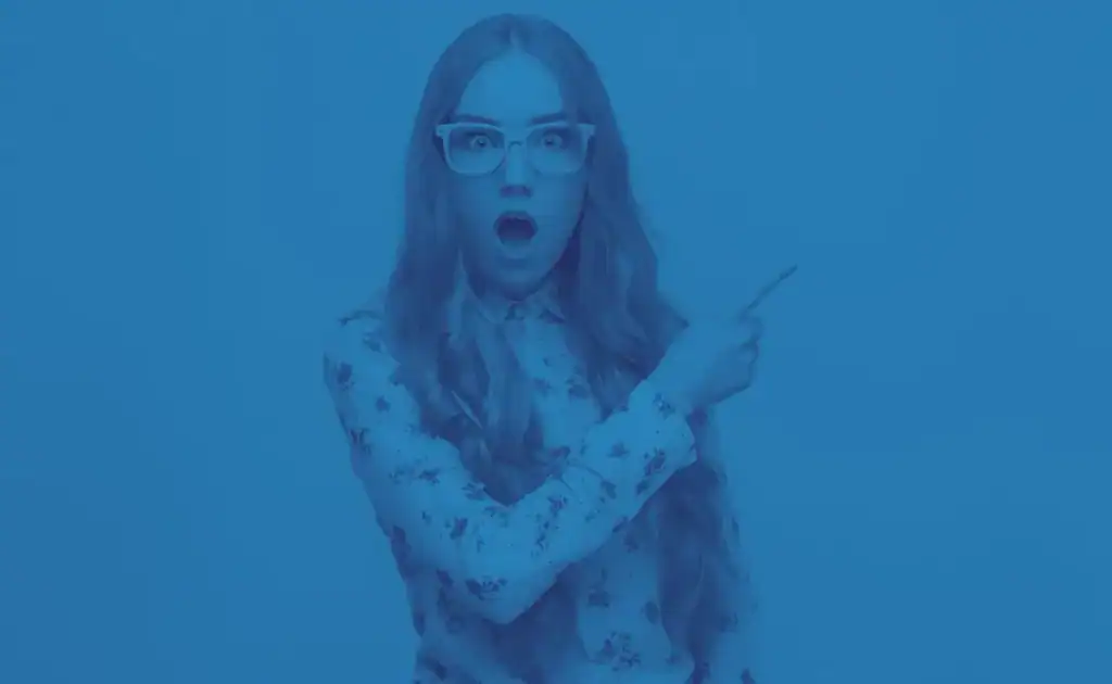 Woman with glasses surprised while pointing at her phone.
