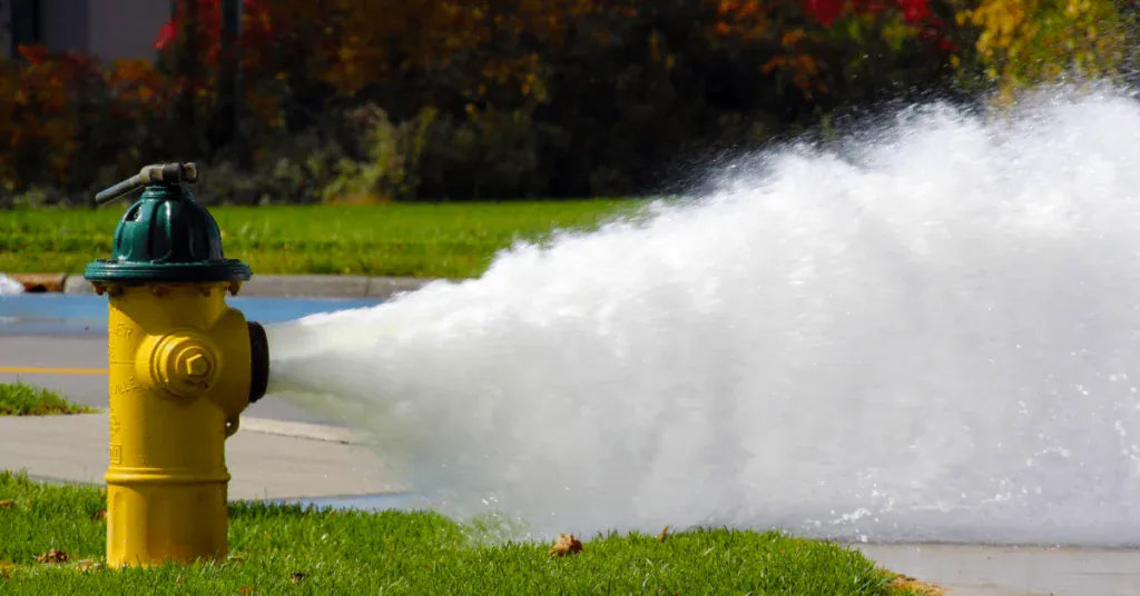 Fire hydrant releasing a powerful stream of water on green grass.