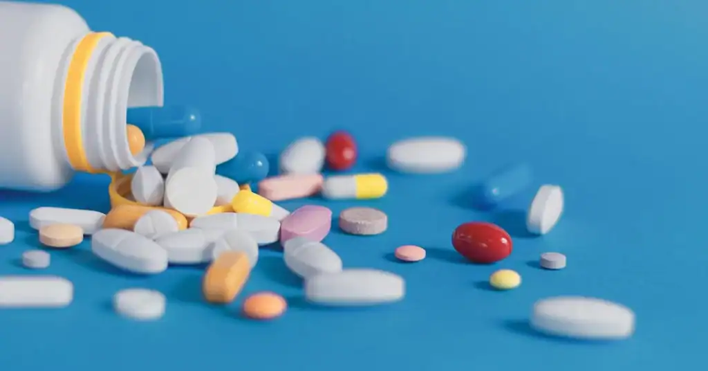 Assorted pills and medication spilling from a bottle on a blue background.